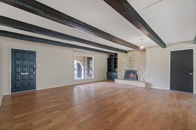 1910 Woodland Ave, Austin, TX 78741 - unfurnished living room with beam ceiling, a large fireplace, wood finished floors, baseboards, and a textured ceiling