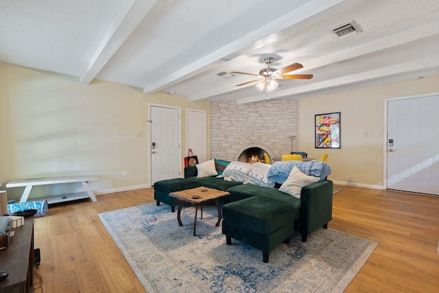 living area featuring a ceiling fan, light wood-style flooring, a fireplace, and beamed ceiling