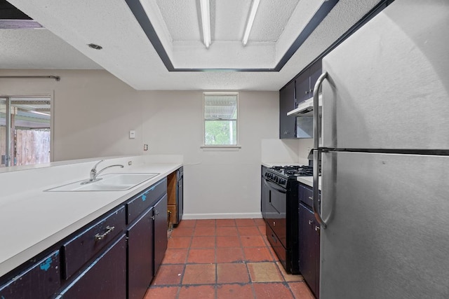 kitchen with black gas range oven, a sink, light countertops, freestanding refrigerator, and under cabinet range hood