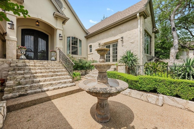 doorway to property featuring french doors, stucco siding, and roof with shingles
