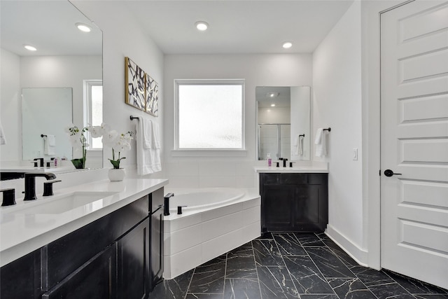 full bathroom with a bath, a shower stall, two vanities, a sink, and marble finish floor