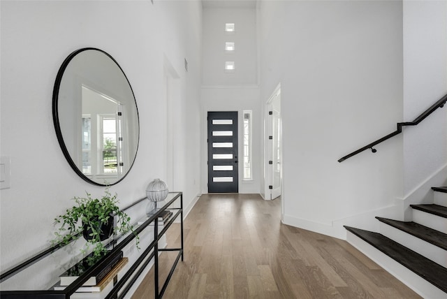 entryway featuring stairs, baseboards, wood finished floors, and a high ceiling