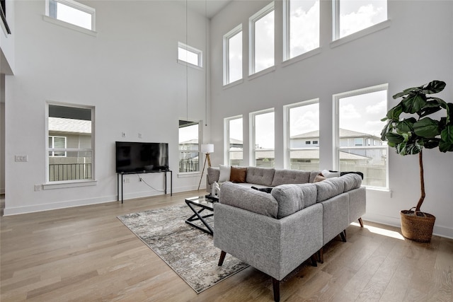 living area featuring light wood-style floors, baseboards, and a towering ceiling