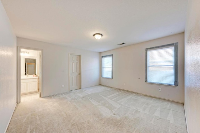 unfurnished bedroom with visible vents, a sink, baseboards, and light colored carpet