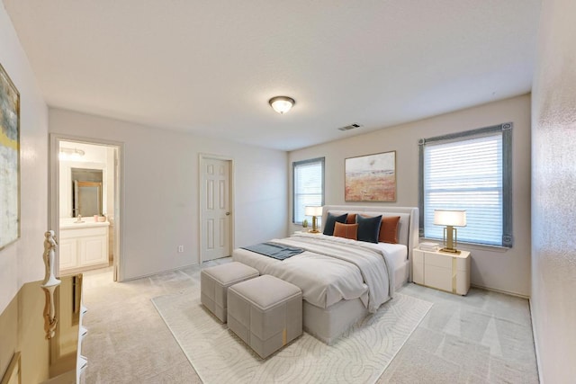 bedroom featuring visible vents, a sink, ensuite bathroom, and light carpet