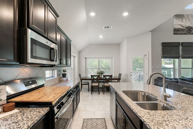 kitchen with decorative backsplash, light stone counters, a sink, appliances with stainless steel finishes, and vaulted ceiling