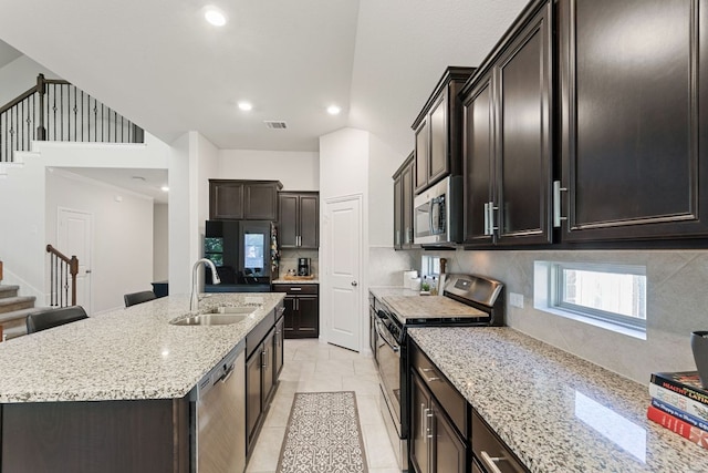kitchen featuring backsplash, appliances with stainless steel finishes, a center island with sink, a sink, and light stone counters