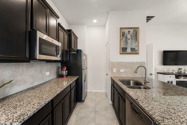 kitchen featuring stainless steel appliances, light tile patterned flooring, stone counters, and a sink