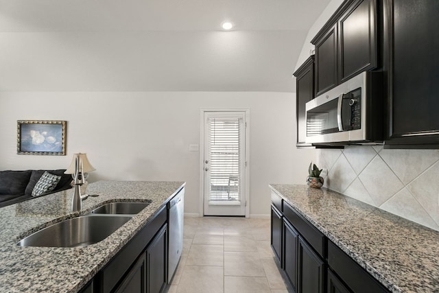 kitchen with decorative backsplash, a sink, stone countertops, dark cabinetry, and stainless steel appliances