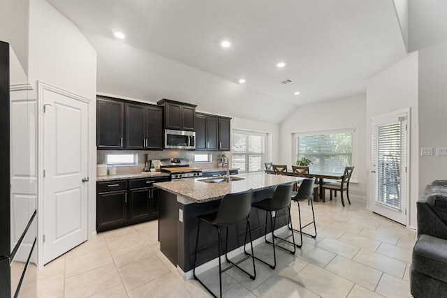 kitchen featuring appliances with stainless steel finishes, a sink, vaulted ceiling, a kitchen bar, and visible vents