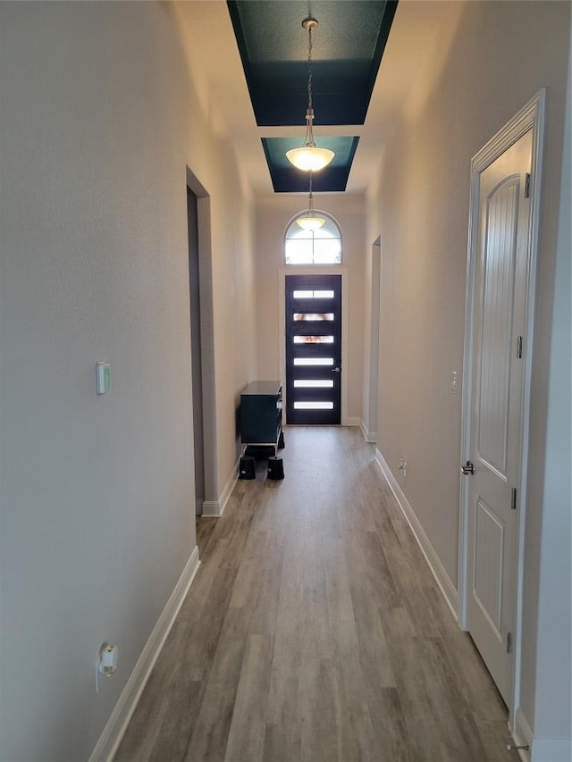 corridor with baseboards, wood finished floors, and a raised ceiling