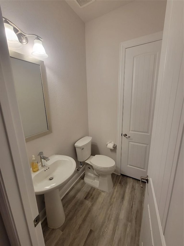 bathroom with toilet, a sink, visible vents, and wood finished floors