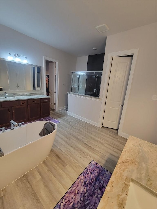full bath featuring vanity, wood finished floors, baseboards, a freestanding bath, and a shower stall