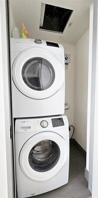 clothes washing area with baseboards, tile patterned flooring, laundry area, and stacked washer and dryer