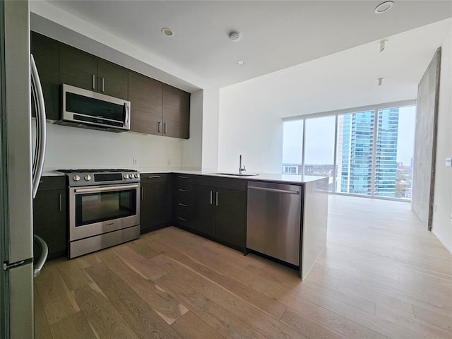 kitchen with a peninsula, light wood-type flooring, light countertops, a sink, and appliances with stainless steel finishes