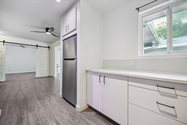 kitchen featuring freestanding refrigerator, light countertops, a barn door, white cabinets, and tasteful backsplash