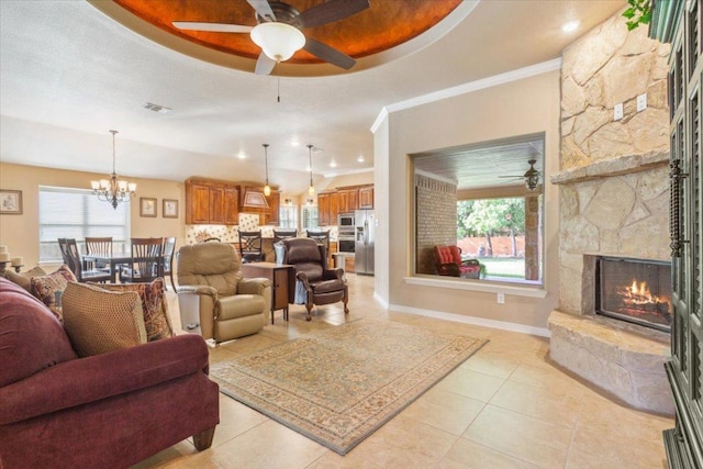 living area featuring baseboards, visible vents, a stone fireplace, and ceiling fan with notable chandelier