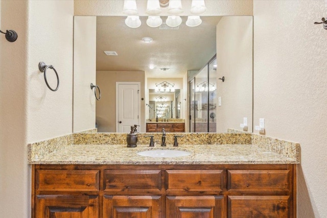 full bathroom featuring a shower with door, a textured wall, and vanity