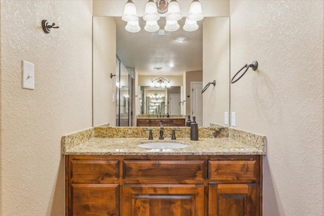 full bath featuring visible vents, a shower with shower door, vanity, a chandelier, and a textured wall