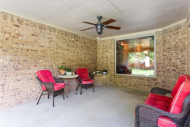 sitting room with carpet, a ceiling fan, and brick wall