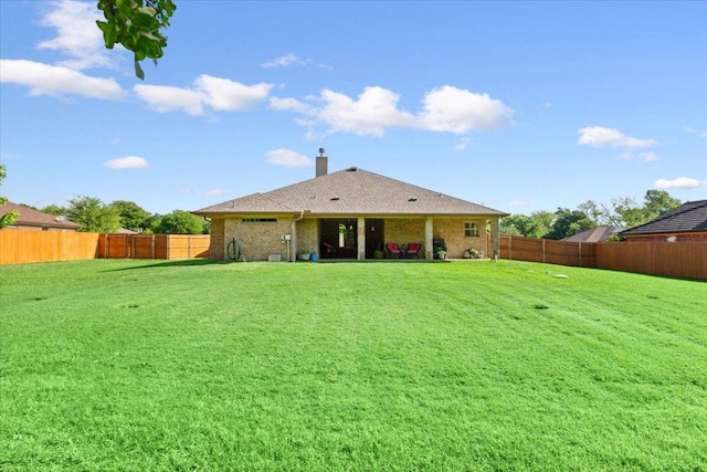 back of house with brick siding, a fenced backyard, a yard, and a chimney