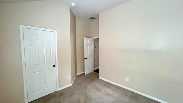 unfurnished bedroom featuring baseboards, carpet flooring, lofted ceiling, and visible vents