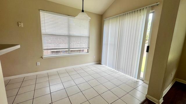unfurnished dining area featuring baseboards, plenty of natural light, vaulted ceiling, and tile patterned floors