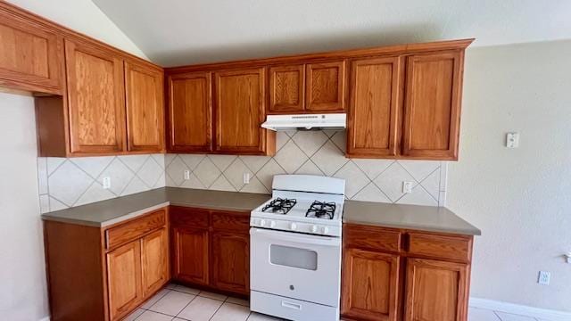 kitchen featuring white gas range, brown cabinetry, under cabinet range hood, and vaulted ceiling
