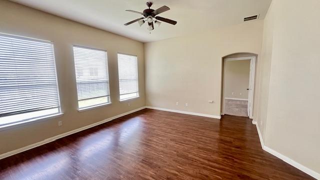 spare room with visible vents, dark wood-style flooring, baseboards, ceiling fan, and arched walkways