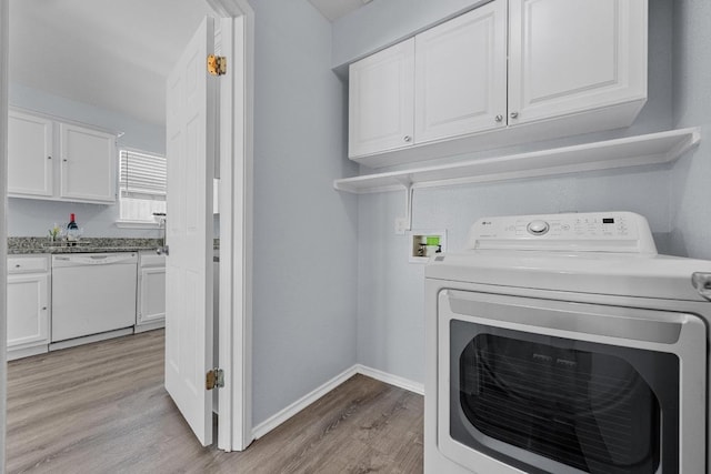 washroom featuring light wood-type flooring, washer / dryer, cabinet space, and baseboards