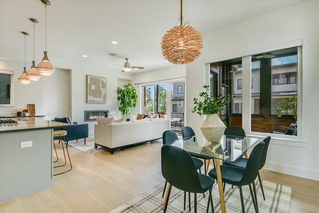 dining area with a ceiling fan, visible vents, light wood-type flooring, a glass covered fireplace, and recessed lighting