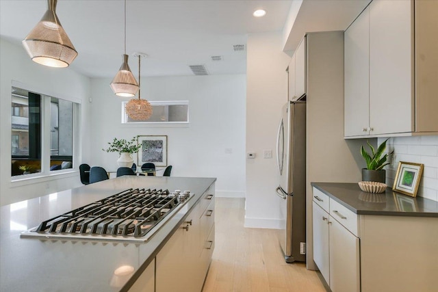 kitchen featuring dark countertops, appliances with stainless steel finishes, light wood-type flooring, tasteful backsplash, and visible vents