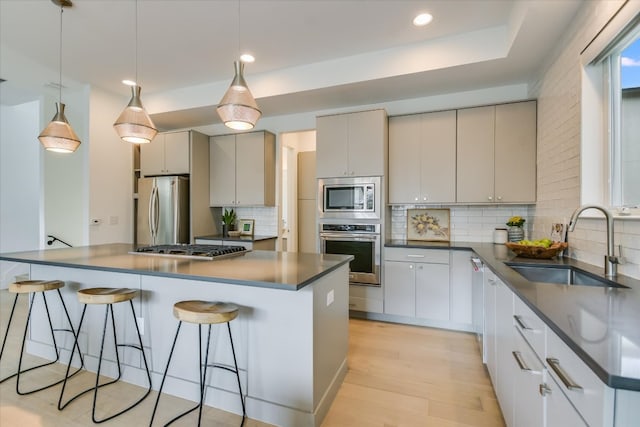 kitchen featuring a kitchen breakfast bar, dark countertops, a sink, light wood-style floors, and stainless steel appliances