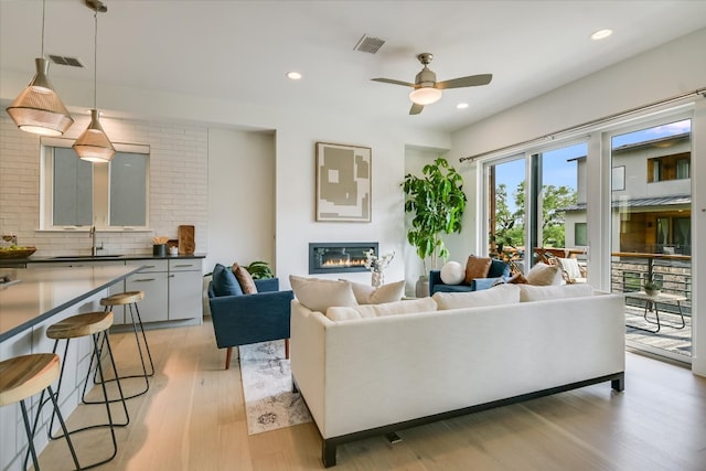 living area featuring visible vents, a ceiling fan, light wood-style floors, and a glass covered fireplace
