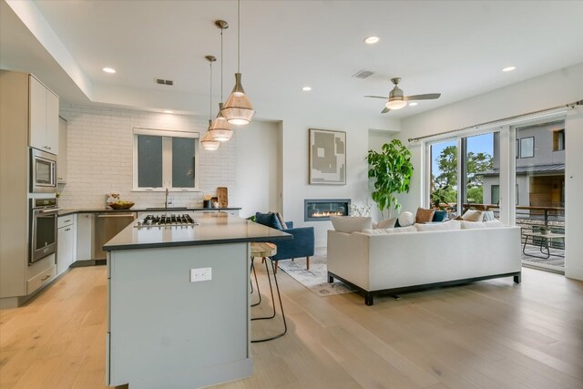 kitchen with a kitchen island, open floor plan, ceiling fan, light wood finished floors, and stainless steel appliances