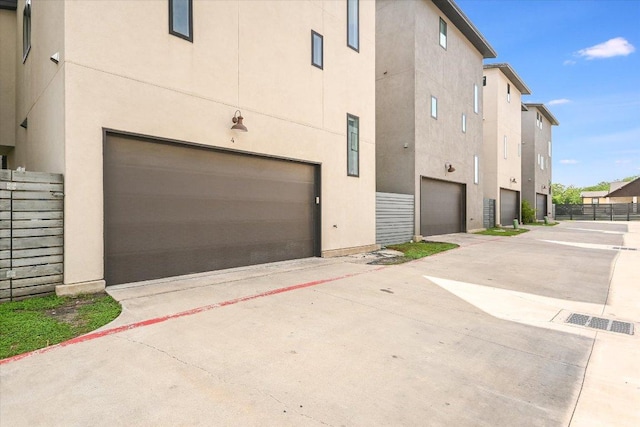 view of property exterior with an attached garage, stucco siding, and fence
