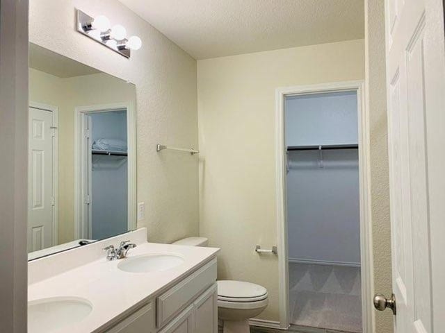 bathroom featuring toilet, double vanity, a textured ceiling, and a walk in closet