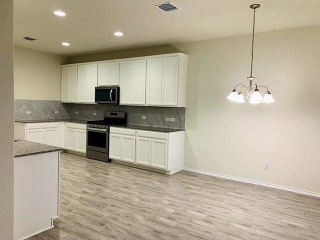 kitchen featuring stainless steel appliances, dark countertops, light wood-type flooring, a chandelier, and decorative backsplash