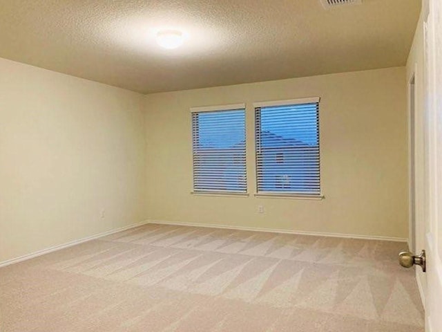 spare room featuring a textured ceiling, light colored carpet, and baseboards
