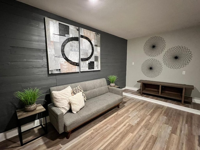 living room featuring baseboards, an accent wall, wood walls, and wood finished floors