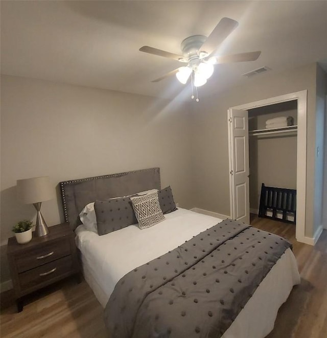 bedroom featuring ceiling fan, visible vents, wood finished floors, baseboards, and a closet