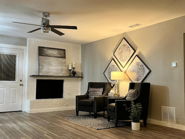 living area featuring a ceiling fan, visible vents, a fireplace, wood finished floors, and baseboards