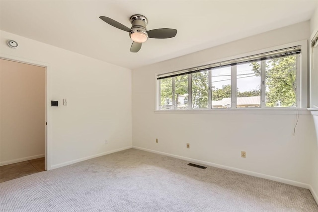 carpeted empty room with baseboards, a ceiling fan, and visible vents