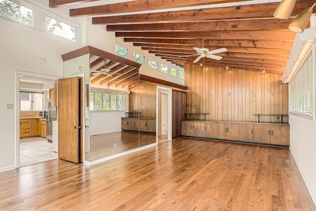 unfurnished living room featuring wooden walls, ceiling fan, beam ceiling, and light wood finished floors