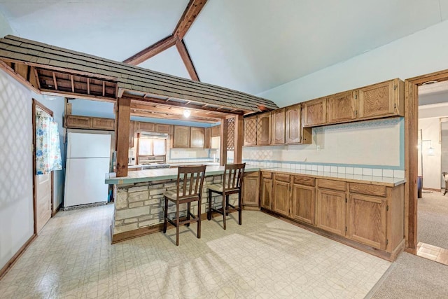 kitchen featuring brown cabinetry, freestanding refrigerator, tile countertops, baseboards, and lofted ceiling