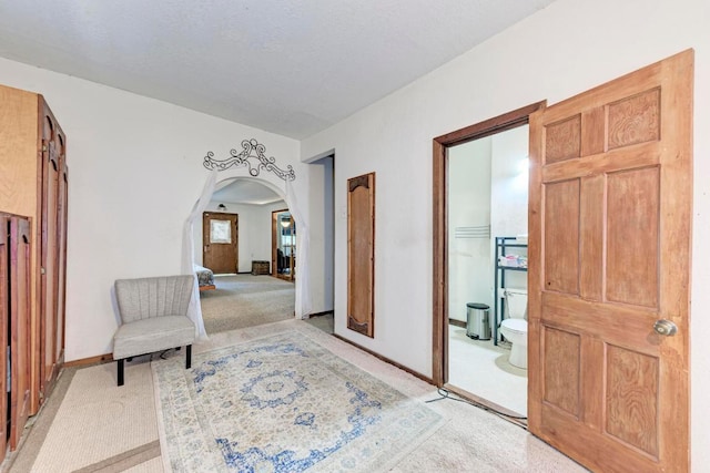 interior space featuring arched walkways, baseboards, and light colored carpet