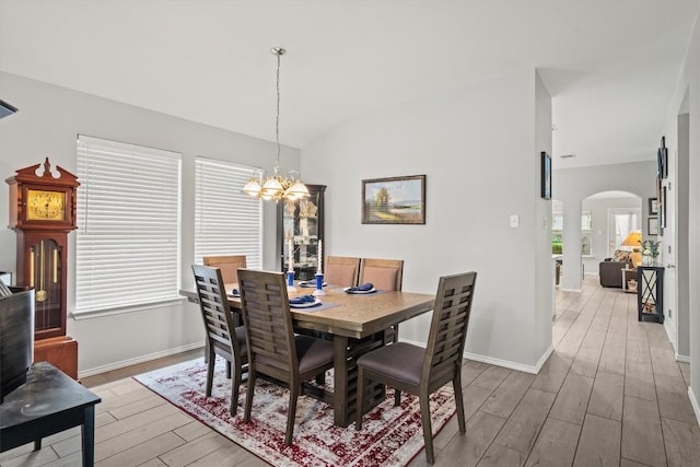 dining space with light wood-type flooring, arched walkways, baseboards, and a notable chandelier