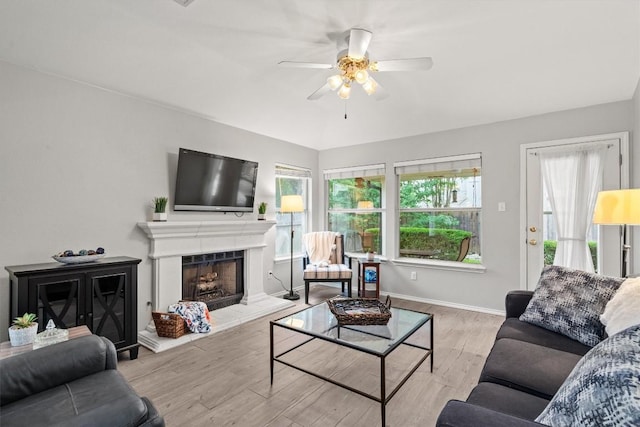living area with baseboards, a fireplace with raised hearth, a ceiling fan, and wood finished floors