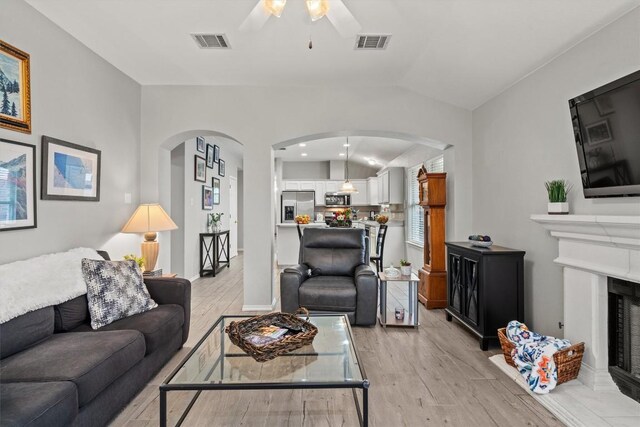 12804 Council Bluff Dr, Austin, TX 78727 - living area featuring arched walkways, light wood finished floors, a ceiling fan, vaulted ceiling, and a fireplace