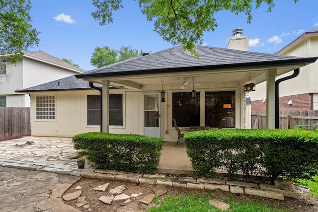 rear view of property featuring fence, a patio, a chimney, and a shingled roof